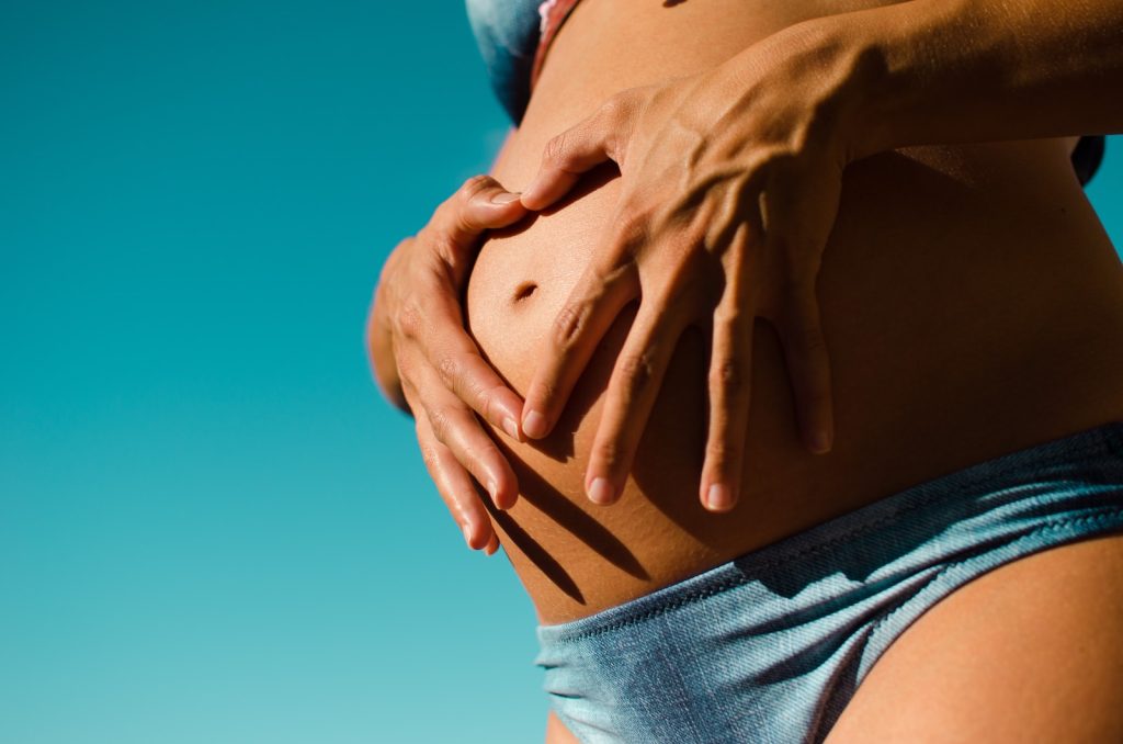 Une femme enceinte en bikini avec les mains sur le ventre.