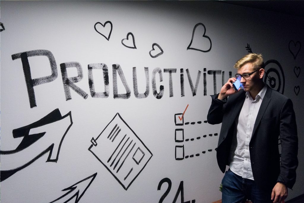 Un homme d'affaires parlant au téléphone devant un mur avec le mot productivité écrit dessus.