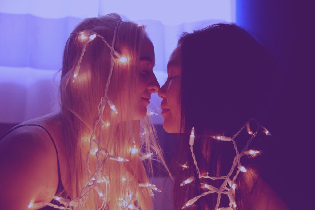 Deux femmes s'embrassant avec des lumières de Noël sur le visage.