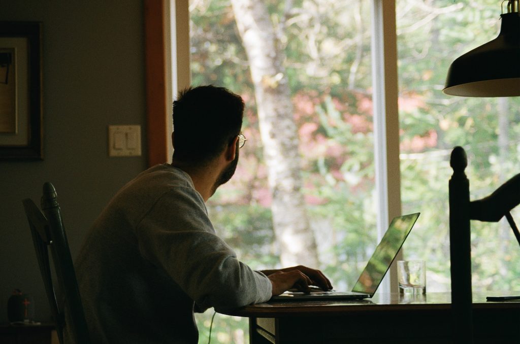 Un homme assis à une table avec un ordinateur portable devant une fenêtre.