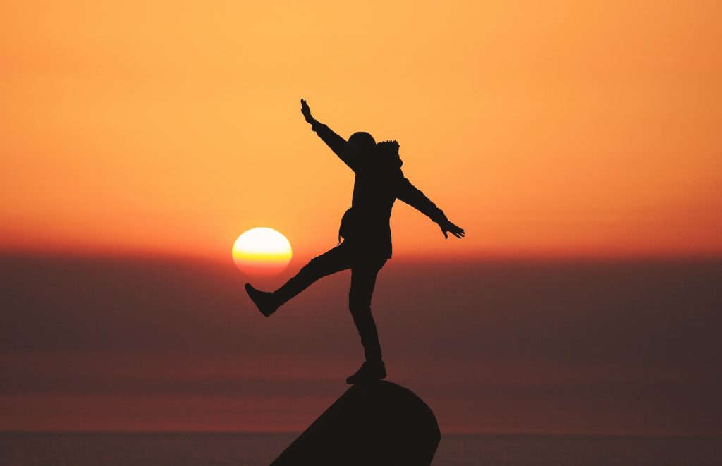 Une silhouette d’une personne debout au sommet d’un rocher au coucher du soleil.