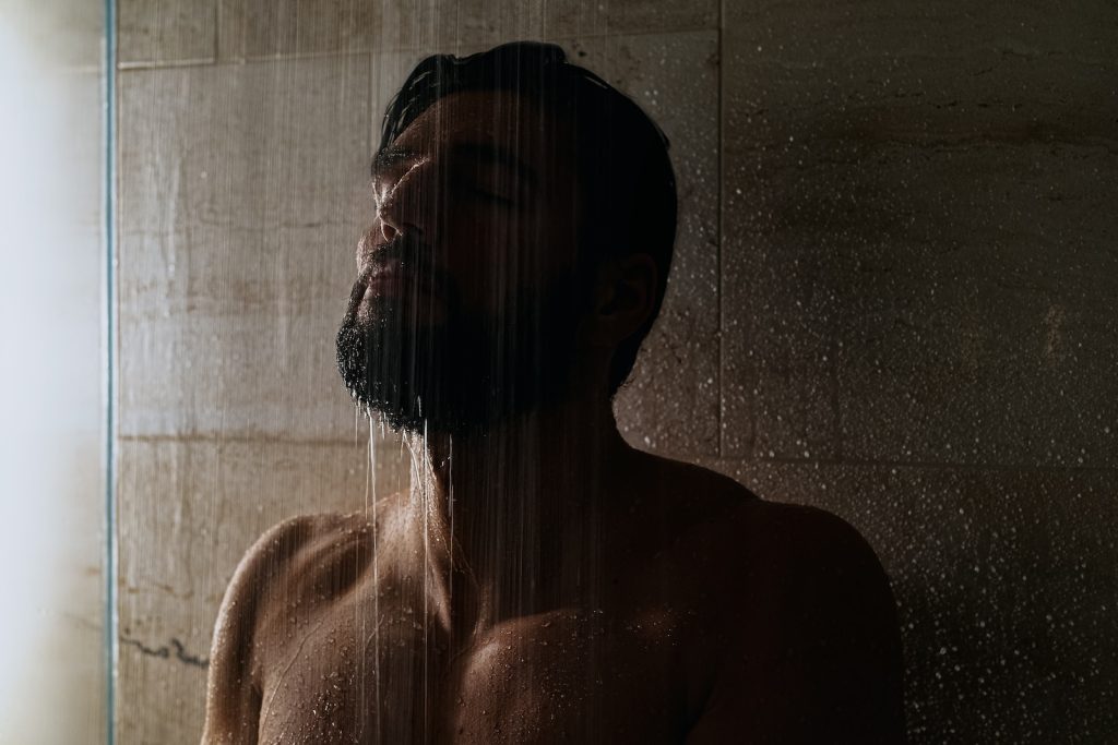 Un homme barbu debout sous la douche.