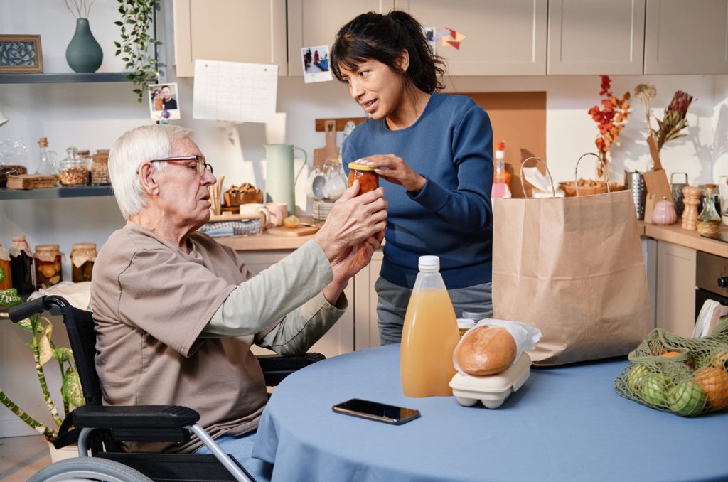 Une femme en fauteuil roulant aide un homme plus âgé dans la cuisine.